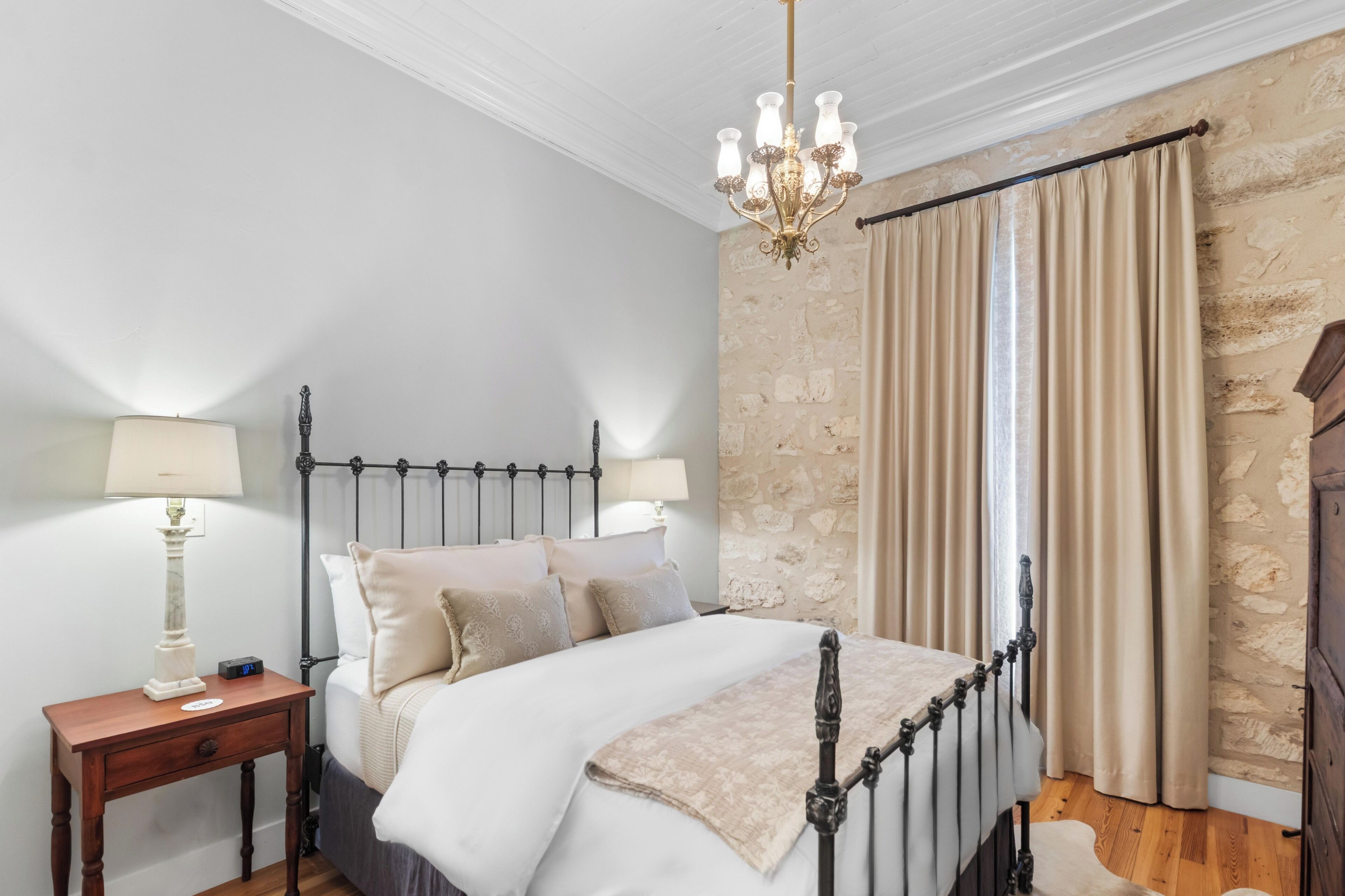 Un dormitorio con cama con dosel, una mesita de noche con lámpara, un candelabro y una pared con textura de piedra.