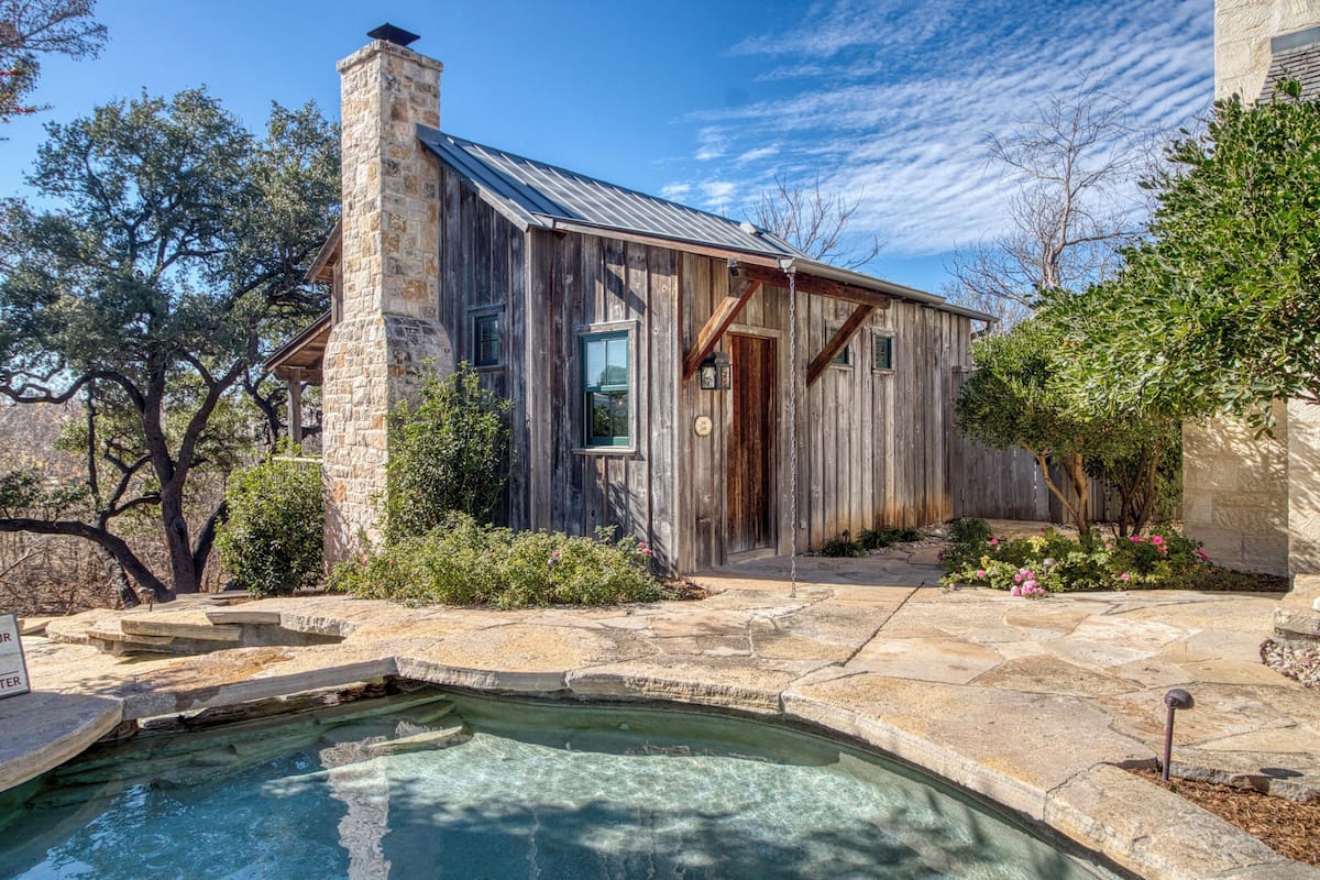 A rustic cabin with a stone chimney, a stone pool, and a wooden deck.