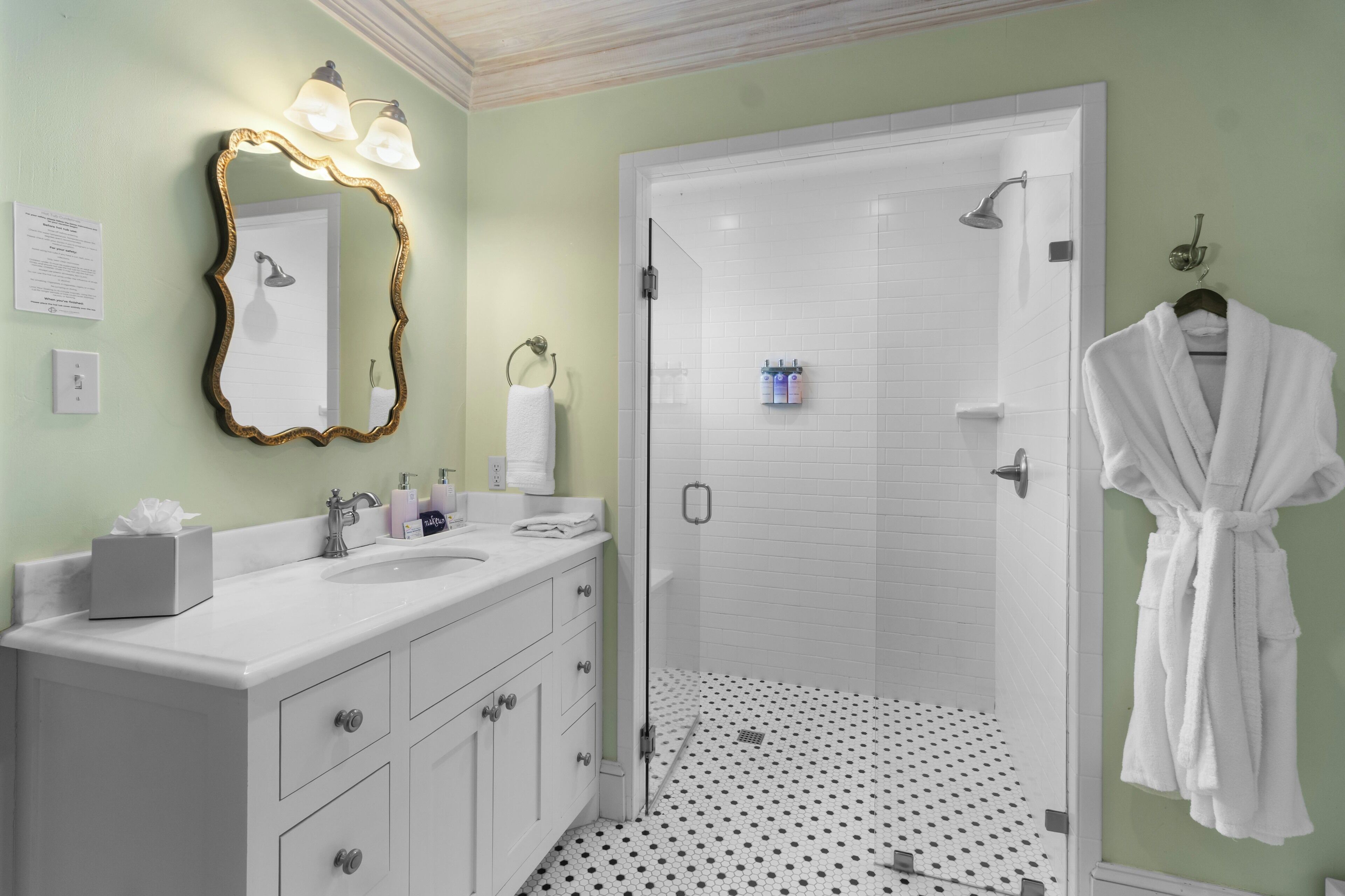 A bathroom with a white vanity, a large mirror with a gold frame, a towel rack, and a white robe hanging on the wall.