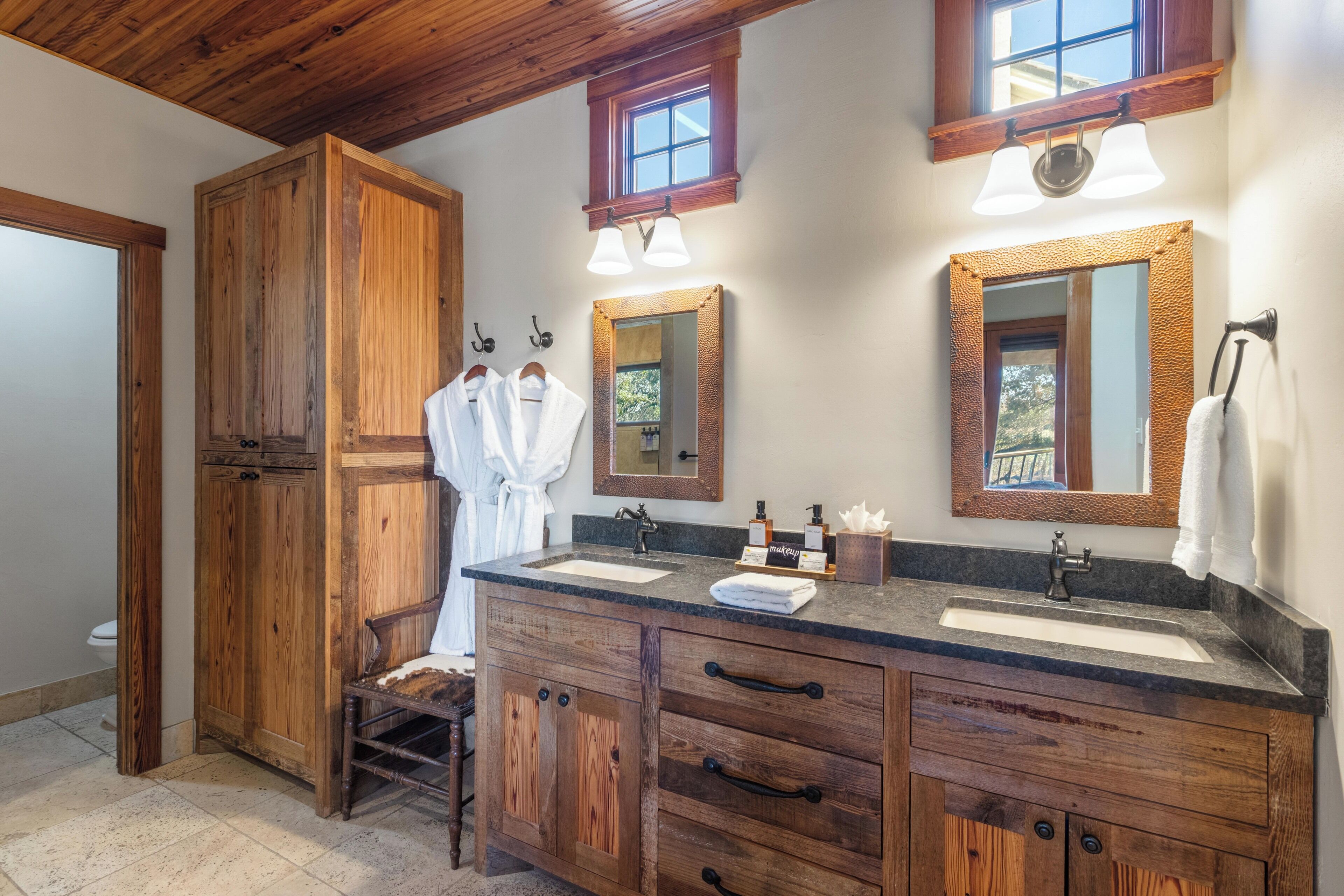 A wooden vanity with a sink, two mirrors, and a towel rack.