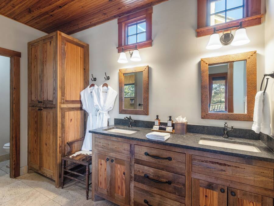 A wooden vanity with a sink, two mirrors, and a towel rack.
