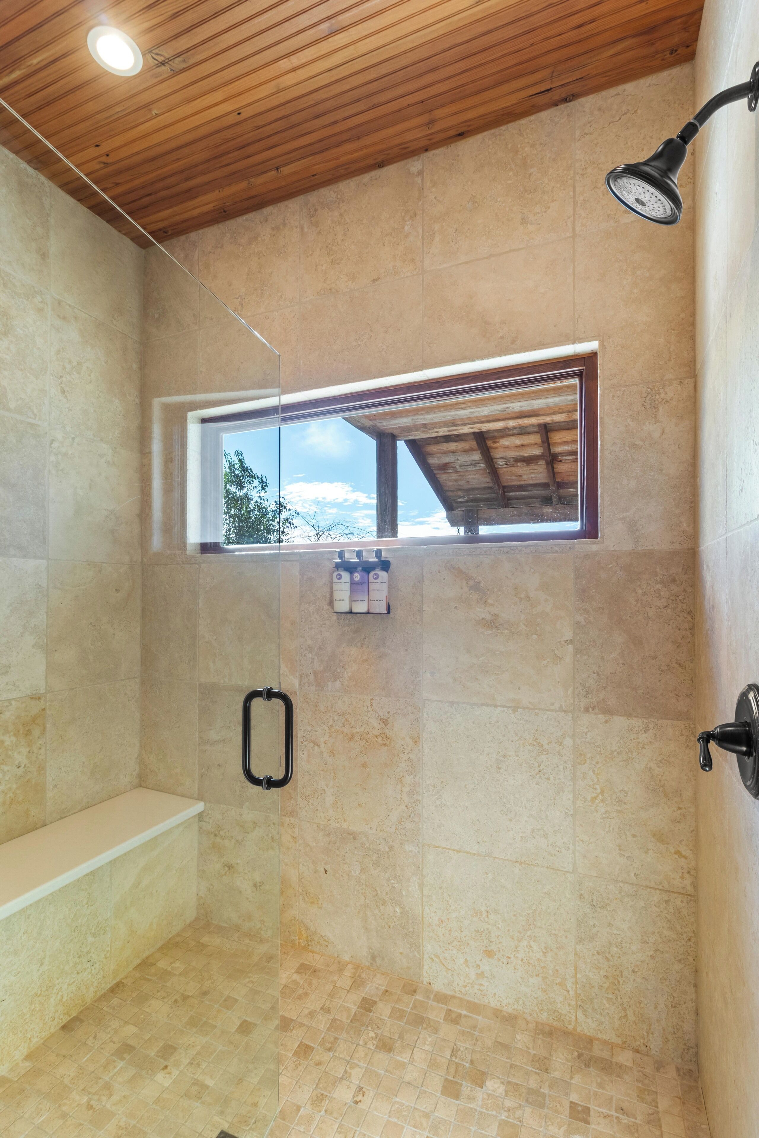 Una ducha con techo de madera, ventana y suelo de baldosas.