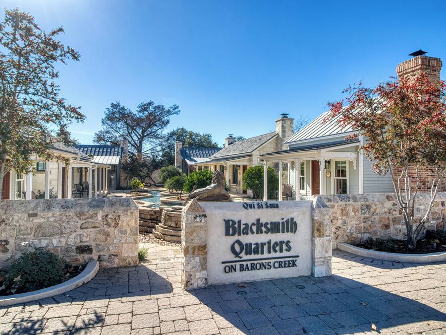 A sign for Blacksmith Quarters on Barons Creek with a stone wall and a small garden area.