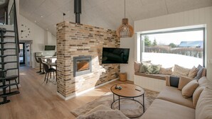 Ein modernes Wohnzimmer mit Kamin aus Ziegelsteinen, einem großen, an der Wand montierten Fernseher, einer Couch und einem Essbereich mit Tisch und Stühlen.