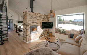 Un salon moderne avec une cheminée en briques, un grand téléviseur fixé au mur, un canapé et un coin repas comprenant une table et des chaises.