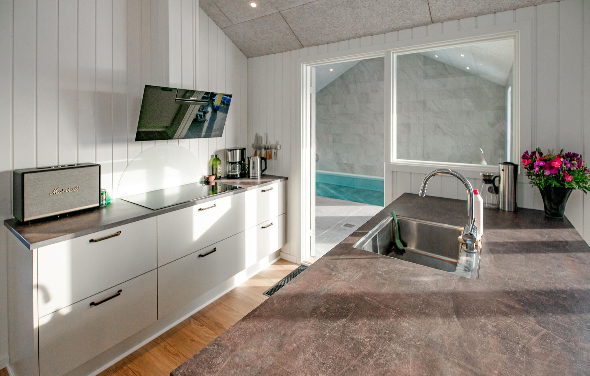 Una cocina moderna con armarios blancos, un ventanal y vistas a una piscina.