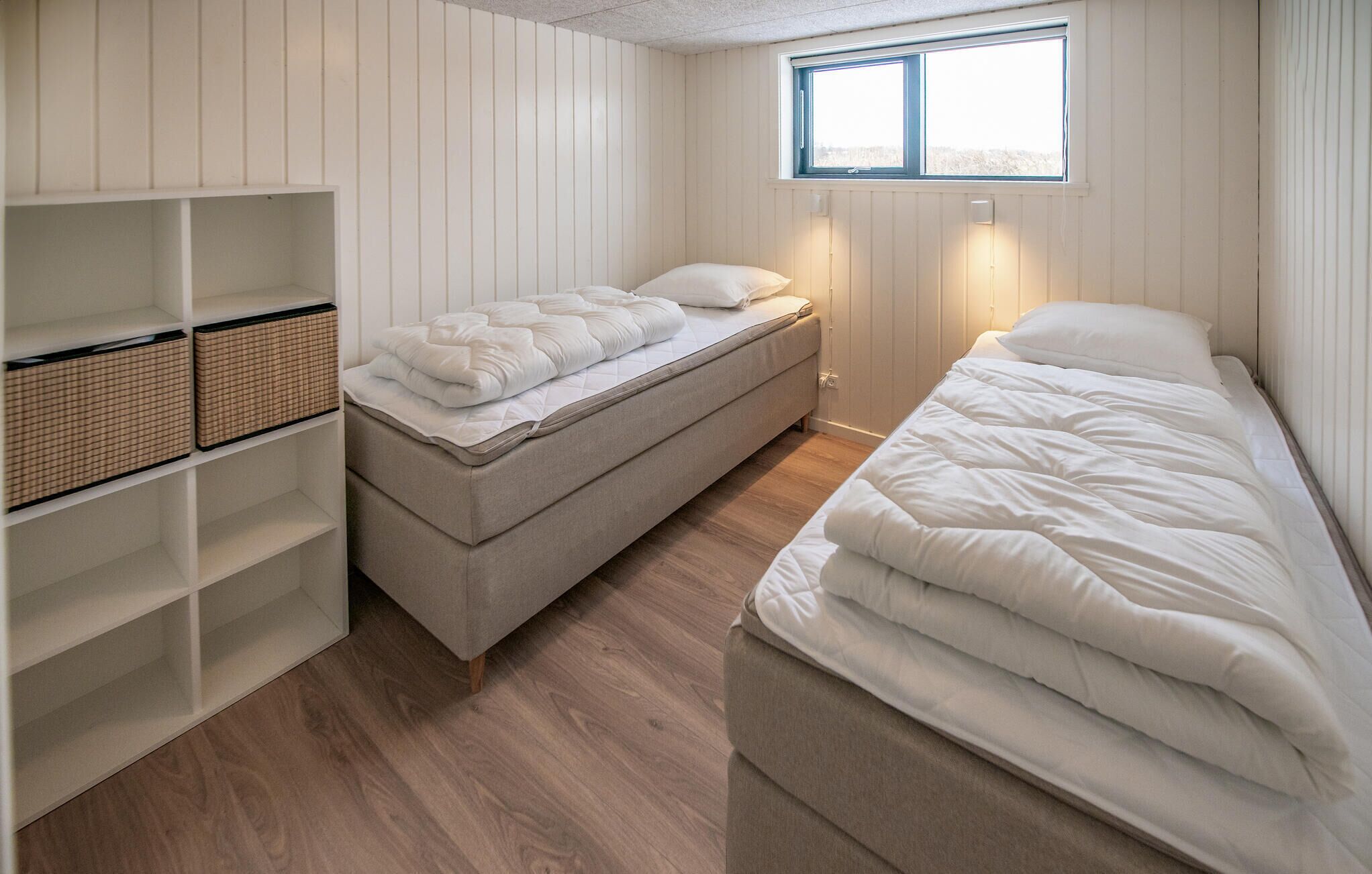Ein kleines, kompaktes Schlafzimmer mit zwei Einzelbetten, einem Einbauschrank und einem Fenster, das für natürliches Licht sorgt.