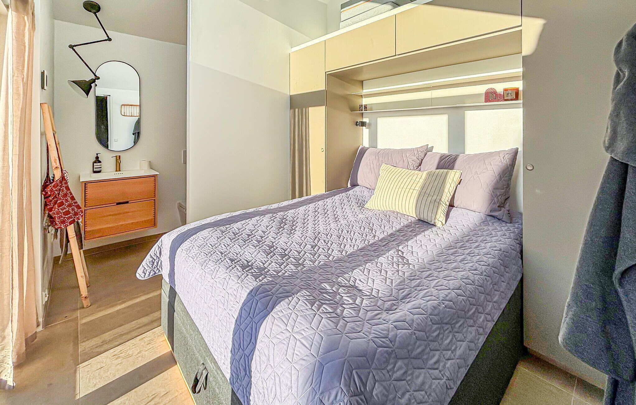 A bedroom with a bed, a dresser, a mirror, and a hanging bag.