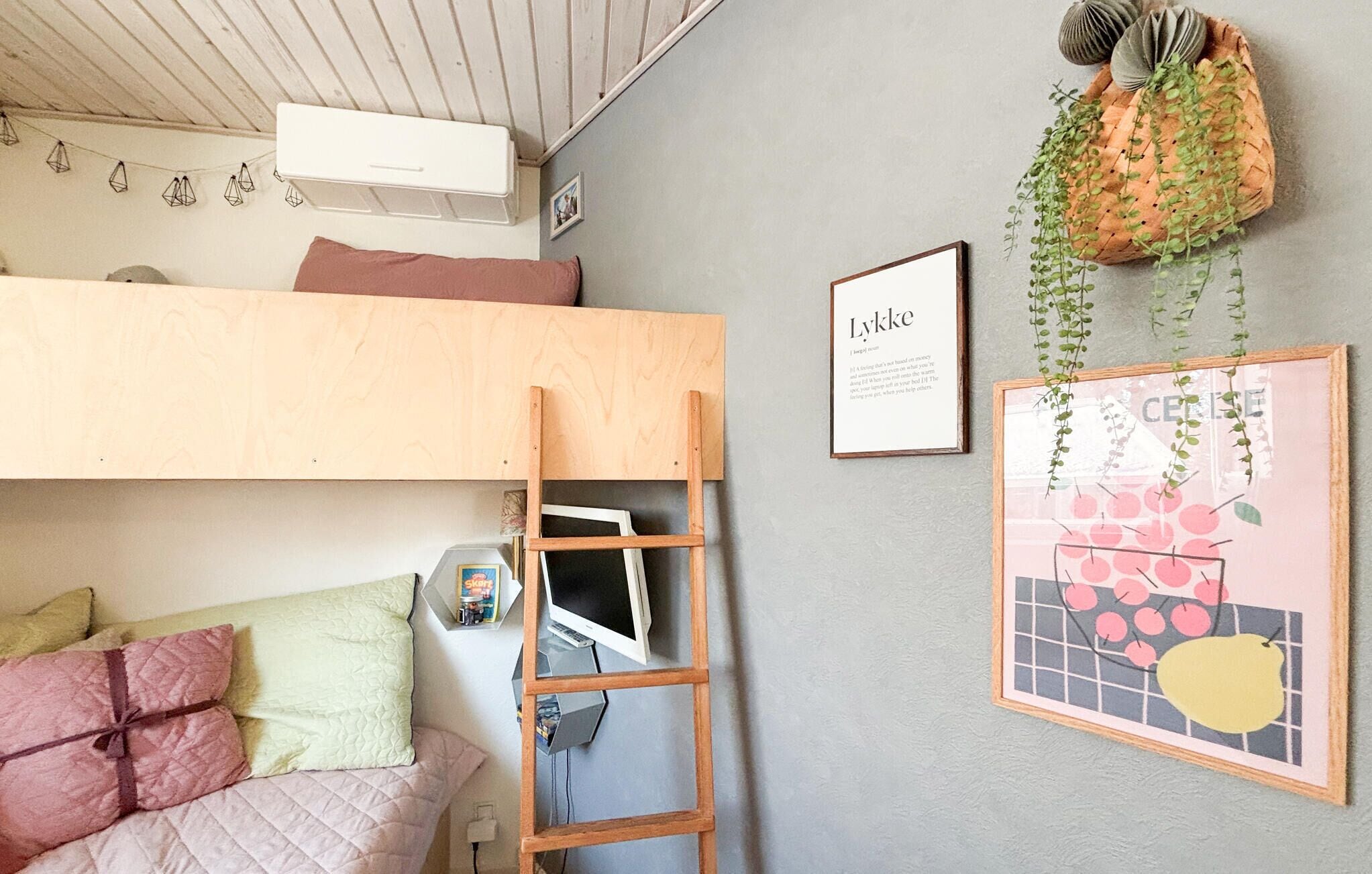 Ein gemütliches Schlafzimmer mit einem Etagenbett, einer Leiter, einem Schreibtisch mit einem Laptop und einem gerahmten Bild an der Wand.