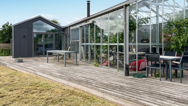 A modern house with a large glass conservatory, a deck with outdoor furniture, and a chimney.