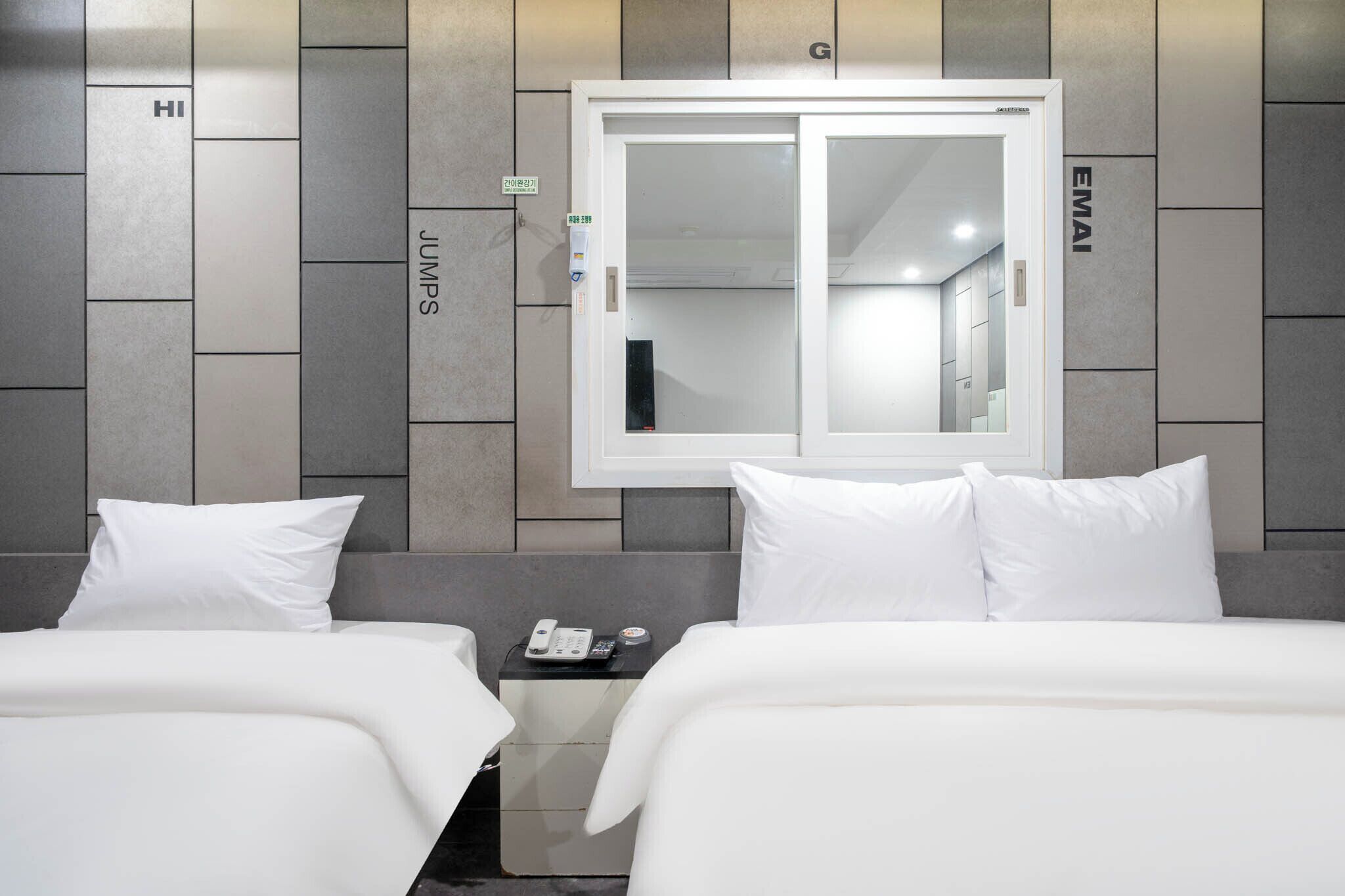 Habitación de hotel con dos camas, una mesita de noche con un teléfono y un espejo grande en la pared.