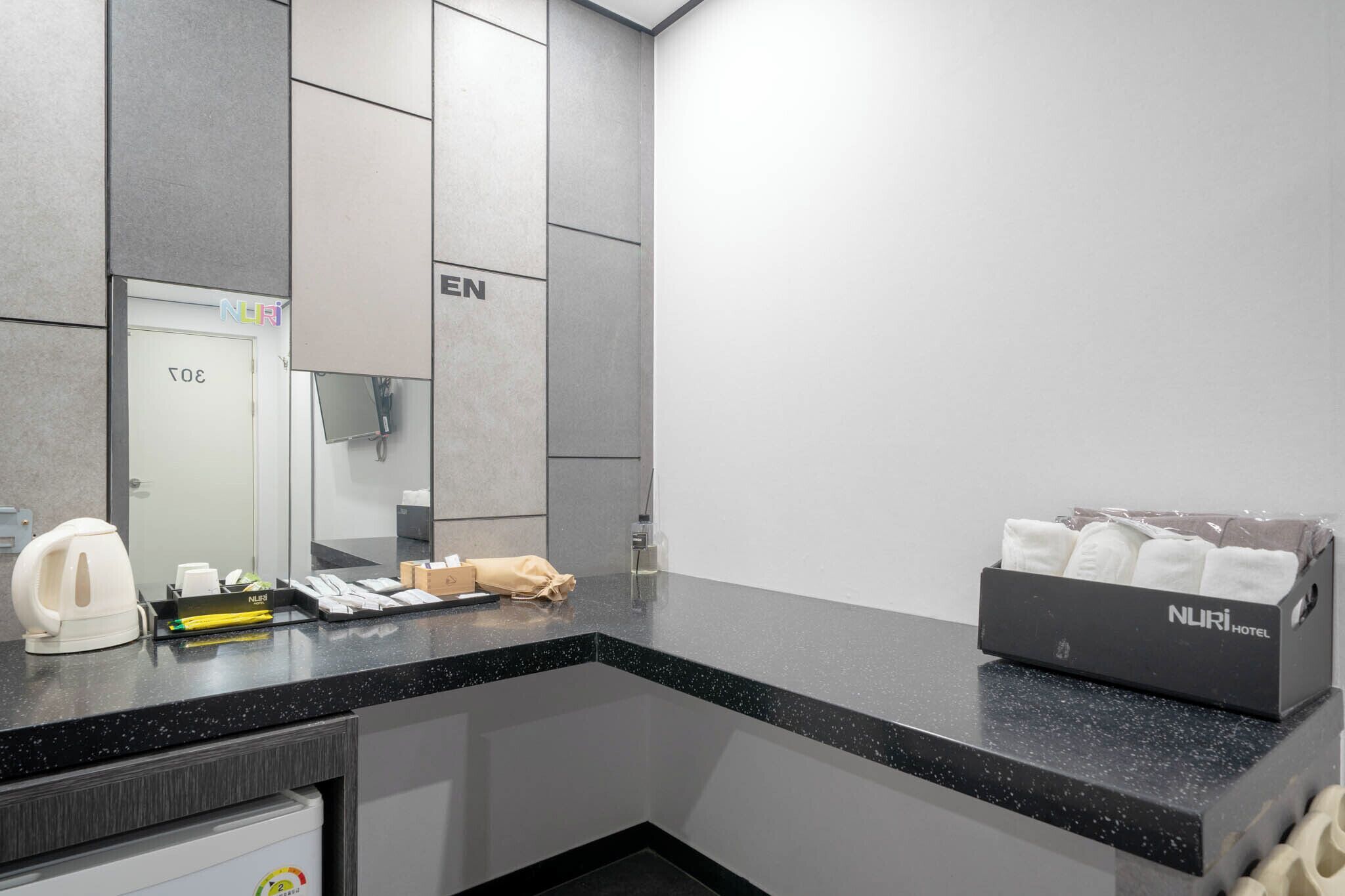 A modern hotel bathroom with a black countertop, a mirror, a towel rack, and a NURI HOTEL sign.