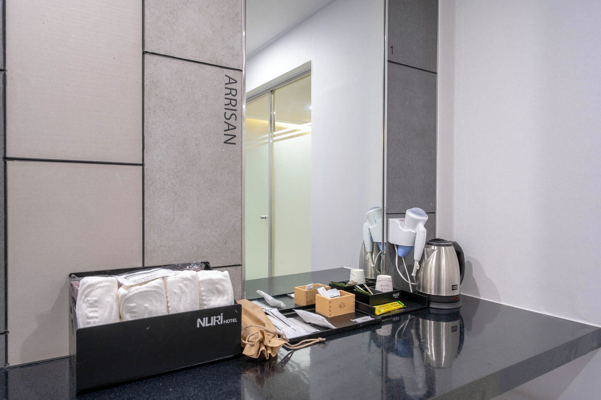A hotel room with a black minibar, a mirror, a glass door, and a counter with toiletries and a kettle.