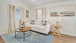 A living room with a white sofa, a round coffee table, a blue rug, a ceiling fan, and a painting on the wall. - Cottage on Camden 8 - Downtown! (Stuart)