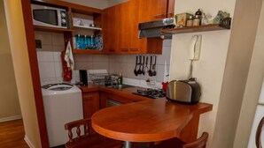 A compact kitchen with wooden cabinets, a built-in microwave, a toaster, and a sink. - Central and comfortable apartment in Santiago Centro. (Santiago)