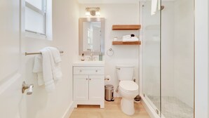 Un baño moderno con cabina de ducha de vidrio, inodoro blanco, tocador con espejo y un perchero para toallas.