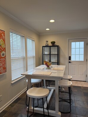 A dining area with a white table, four stools, a black cabinet with glass doors, and a door with a window. - Acorn Cottage a Peaceful 3-bedroom house 1 mile from Elon University (Elon)