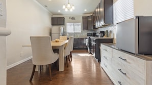 A modern kitchen with a dining area, wooden cabinets, a stainless steel refrigerator, and a chandelier. - 3-bedroom house in central San Antonio with AC for comfort (San Antonio)
