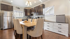 A modern kitchen with dark cabinets, a stainless steel refrigerator, a dining table with chairs, and a coffee-themed wall. - 3-bedroom house in central San Antonio with AC for comfort (San Antonio)