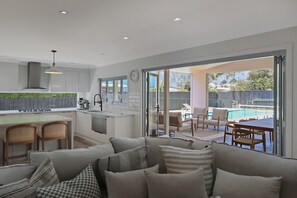 Una cocina moderna con una isla central, un comedor con vistas a la piscina y una sala de estar acogedora con sofá y cojines.