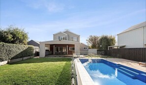 A residential backyard with a swimming pool, a covered patio, and a house with a sloped roof. - Pool House Barwon Heads 4 bedroom, 2 bathroom, sleeping 8, Heated Pool (Barwon Heads)