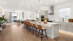 A modern kitchen with a large island, bar stools, pendant lights, and a view to the dining area.