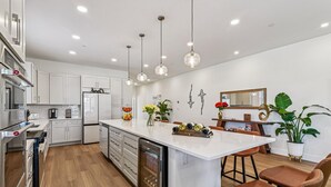 A modern kitchen with white cabinetry, a central island, pendant lights, and a dining area with a wooden table and chairs.