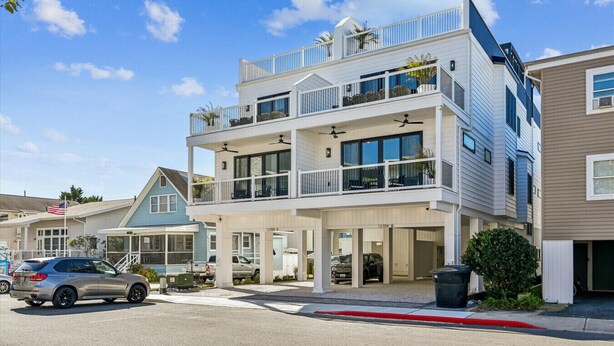 A multi-story residential building with a balcony on the second floor, a garage, and a driveway with parked cars.
