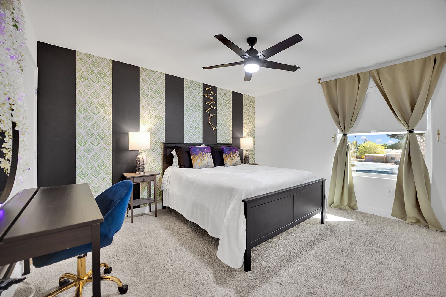 Ein Schlafzimmer mit Bett, Schreibtisch, Stuhl, Deckenventilator und Vorhängen.