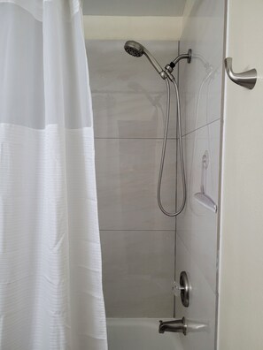 A shower area with a handheld showerhead, a wall-mounted faucet, and a clear shower curtain. - Garden Sanctuary, Mid-term, Peaceful Lake-town Home (Lake Stevens)