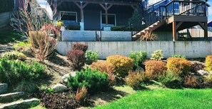 A residential property with a wooden deck, a staircase, and a variety of shrubs and plants.