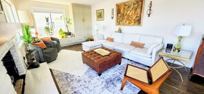 A living room with a fireplace, sofa, ottoman, and a glass coffee table. - Amazing 2-BD waterfront in Kent/Seattle. Dock, BBQ, Paddle boards, Game room!  (Kent)