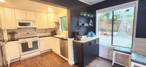 Une cuisine avec des meubles blancs, un four à micro-ondes, un four traditionnel, un lave-vaisselle et une fenêtre donnant sur l’extérieur.