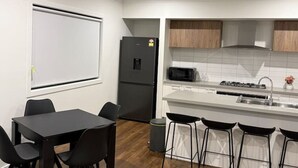 Eine moderne Küche mit weißen Schränken, einem schwarzen Kühlschrank, einer Mikrowelle und einem Waschbecken. Es gibt einen Essbereich mit einem schwarzen Tisch und Stühlen.