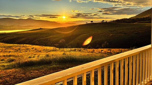 A scenic view from a balcony with a wooden railing, overlooking rolling hills and a sunset. - Large Group Lodge with Breathtaking Montana Views (cardwell)