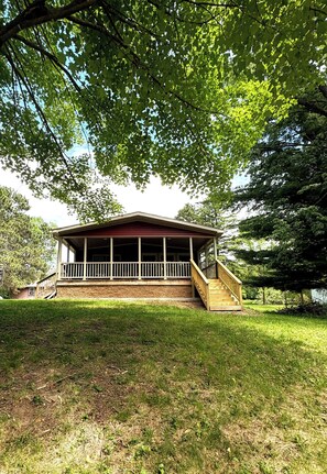 Une cabane en bois avec un porche, entourée d’arbres.