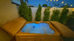 A hot tub with two side seats and a wooden cover, surrounded by a white brick wall and green plants. - Chic & Cozy Retreat w/Pool+Spa /Close to Old Town! (Scottsdale)