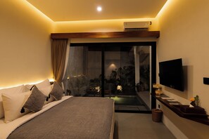 A bedroom with a bed, a TV, a sliding glass door leading to a balcony, and a small table with a plant. - Sedari Villas Ubud (Ubud)