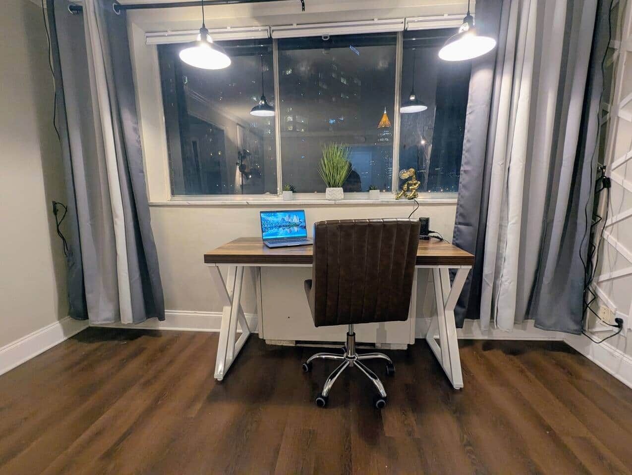 Quarto com escrivaninha, cadeira e janela com cortinas.