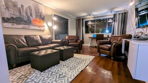 A living room with a brown leather sofa, two leather armchairs, a patterned rug, and a cityscape painting. - ATL City Escape: Work & Play (Atlanta)