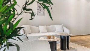 A modern living room with a white sofa, two round tables, and a large potted plant. - Oceanview 2-bedroom Apartment in Bonaire (Kralendijk)