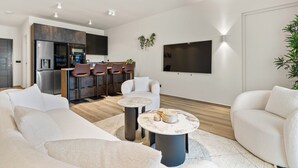 A modern living room with a sofa, two coffee tables, and a kitchen area with a refrigerator, oven, and bar stools. - Oceanview 2-bedroom Apartment in Bonaire (Kralendijk)