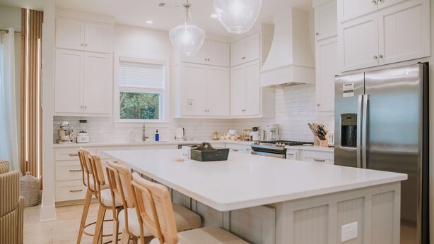 Una cocina moderna con armarios blancos, una isla grande con taburetes de bar, electrodomésticos de acero inoxidable e iluminación colgante.