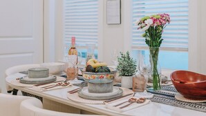 Una mesa de comedor preparada con platos, tazones, cubiertos y un jarrón con flores.