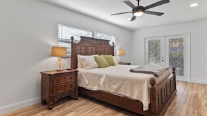 Quarto com cama de madeira, mesas de cabeceira, ventoinha no teto e janela com persianas.