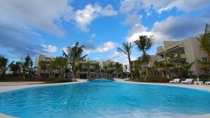 Een resort zwembad met palmbomen en moderne gebouwen op de achtergrond.