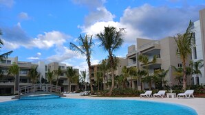 Een zwembadgedeelte van een resort met helderblauw water, palmbomen en moderne gebouwen.