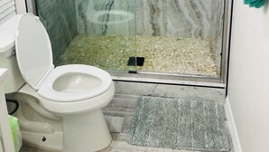 Eine Duschkabine mit Glastüren, ein Marmor-Innenraum, eine Toilette mit weißem Deckel und ein grüner Teppich auf dem Boden.
