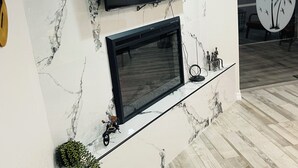 Ein modernes Wohnzimmer mit Fernseher über einem Kamin, Marmorwand und Holzboden.