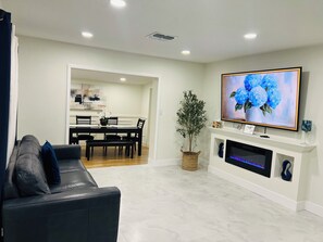 A living room with a black leather sofa, a flat-screen TV mounted above a fireplace, and a dining area in the background. - A Cozy Getaway Just 3 Minutes from the Casino (Tampa)